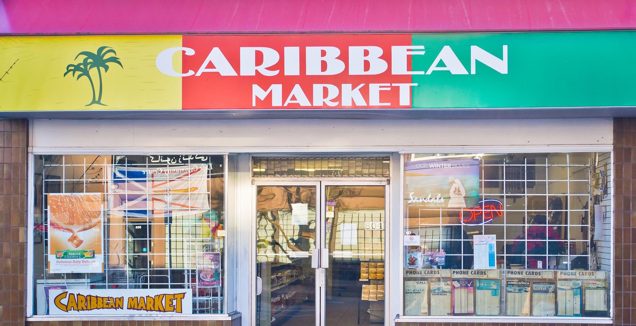  storefront of a Caribbean Market with colorful sign and glass windows.